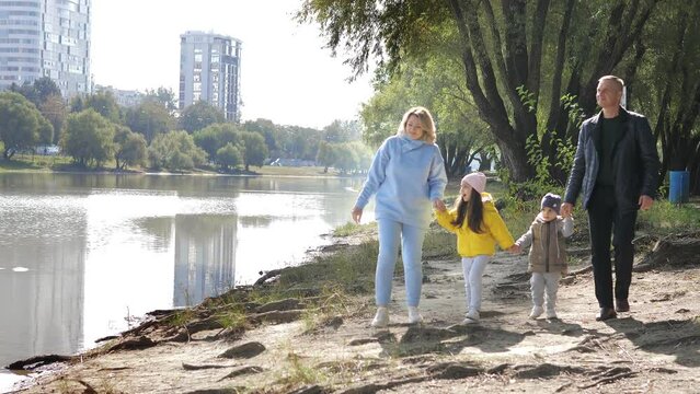 Young couple of grandparents with two little grandkids walking along river shore holding hands in autumn sunny day.Spend leisure time together outdoors for carefree lovely family happiness, recreation