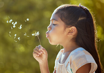 Spring, freedom and girl blowing dandelion flowers for hope, growth and environment in park. Happy,...