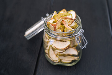 Dried apple slices in open glass jar. Homemade organic dried apple chips with fresh apple on black table background. Sweet vegan snack. Healthy and nutrition concept. Shallow depth of field