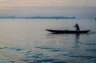 La silhouette di un uomo che voga in piedi sulla sua barca il tramonto e Venezia sullo sfondo