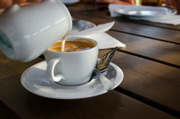Milch gießen in die Tasse mit Kaffe