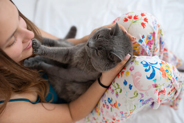 Fototapeta na wymiar Pretty young girl playing with her British shorthair cat in her bed
