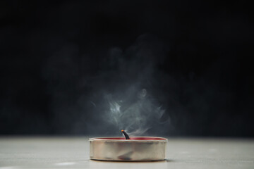 A extinguished candle emitting smoke standing on the table, a black background. Soft selective focus