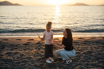 Mother and daughter having fun on the beach at sunset.