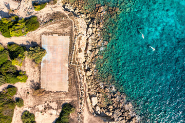 Vista aerea top down di un vecchio campo da calcio tra gli scogli e il mare blu con due uomini che...