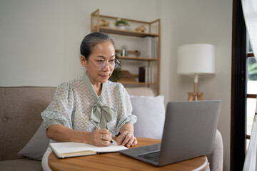 Relaxed Elderly Woman Spending Time With Digital Tablet On Couch In Living Room, Browsing Internet Or Reading News, Side View