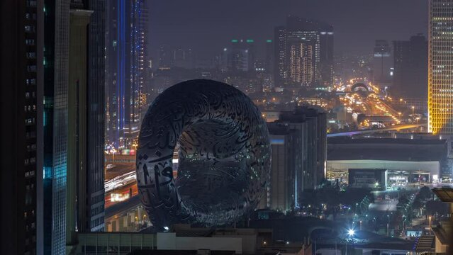 Museum of the Future exhibition space aerial day to night transition timelapse with iconic torus shape. Facade of stainless steel and windows that form an Arabic poem after sunset