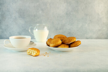 Delicious snack: a cup of black tea with milk and a plate of cookies on a gray background.