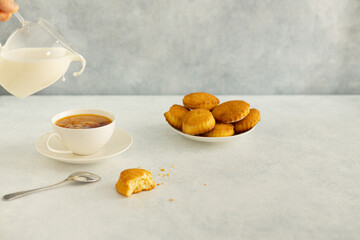 Delicious snack: a cup of black tea with milk and a plate of cookies on a gray background.