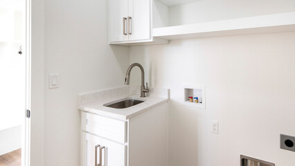 Panorama Empty laundry room with single vanity sink, wall cabinets and shelves