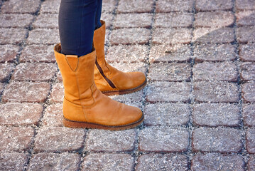 Woman feet in suede boots on salted pavement. Yellow suede shoes and salted pavement, road salt can...