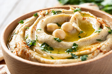 Chickpea hummus in a wooden bowl garnished with parsley, paprika and olive oil on wooden table