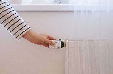 Woman regulates temperature at home with the heating thermostat to save energy, close-up with hand....