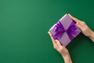 Christmas Eve concept. First person top view photo of female hands giving lilac giftbox with purple ribbon bow on isolated green background with blank space