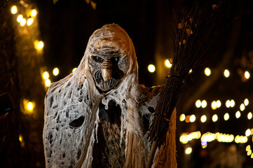 Witch with a broom and a monster face on a dark halloween horror night, bokeh light background