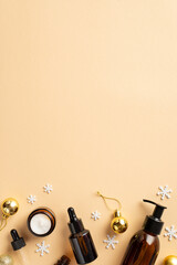 Winter season skincare concept. Top view vertical photo of amber pump bottle cream jar dropper bottle golden baubles and snowflakes on isolated beige background with empty space