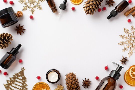 Winter skincare products concept. Top view photo of glass bottles golden ornaments pine cones mistletoe berries anise and dried orange slices on isolated white background with copyspace in the middle