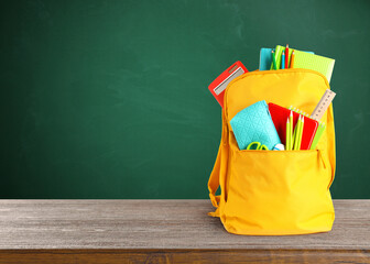 Backpack with school stationery on wooden table near green chalkboard, space for text © New Africa