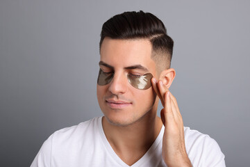 Man applying dark under eye patch on grey background