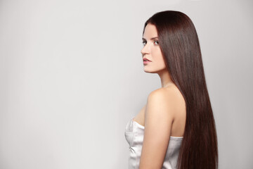 Portrait of beautiful young woman with healthy strong hair on light gray background, space for text