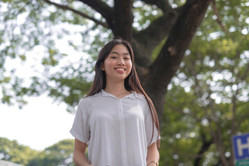 An Asian woman smiles for the camera outside the park on a sunny morning.