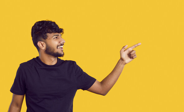 Cheerful Indian guy presenting you good offer or promotional deal by pointing on copy space on banner background. Portrait of young man pointing with his index finger to content on orange background.