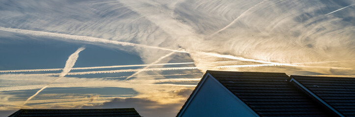 Unusual skyscape with clouds and contrails over rooftops. Devon, UK in October. Sun rising.