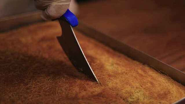 Pastry chef carefully cuts with a knife into the slices of kadaifi baked dessert in the large baking tray