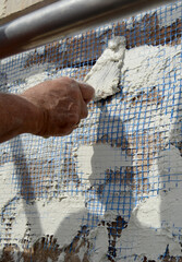 Bricklayer reinforcing the lining of a brick wall with fiberglass mesh and white cement mortar