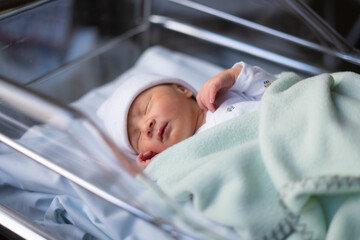 Close up portrait of adorable little newborn baby girl lying quiet at hospital crib hours after...