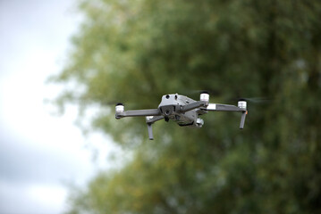 An unmanned quadcopter with a digital camera flies over the green field in summer.