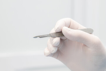 scalpel in the surgeon's hand close-up. a sterile glove on the hand.