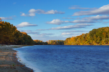beautiful nature, autumn landscape - river and forest with bright sunlight, shadows from clouds on trees, yellow autumn color of leaves