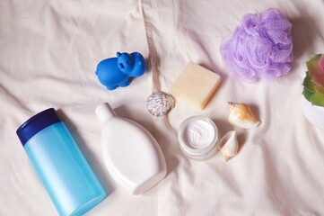 Baby care cosmetic products flat lay photography. Blue shampoo bottle, shower gel, cream, soap bar, purple sponge and toy hippo