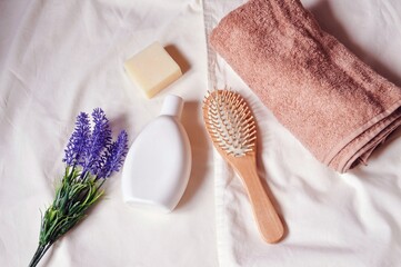 Fototapeta na wymiar White shampoo bottle, natural soap, wooden comb, beige towel and lavender flowers top view photo. Organic cosmetic products for hair and skin care