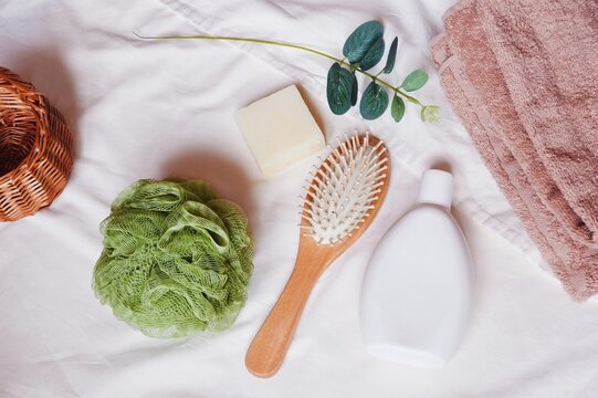 White shampoo packaging, wooden comb, natural soap, green sponge, beige towel and eucalyptus leaves. Bath products on a table flat lay photography