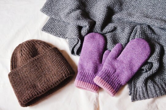 Brown wool hat, purple gloves and gray knitted scarf flat lay fashion photo. Warm clothes for winter weather