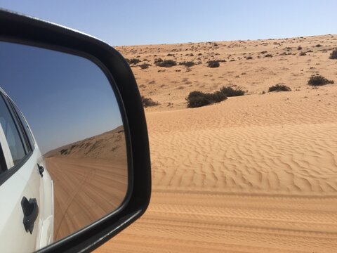 Reflection of road through sand dunes in a car wing mirror, Wahiba Sands, Oman