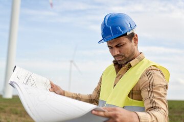 Latin male engineer standing on wind turbine field and checking paper project