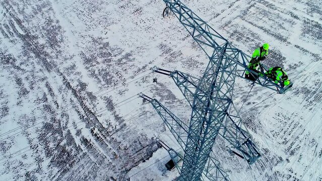 Aerial tilt up shot of worker installing electricity pylon in winter landscape 