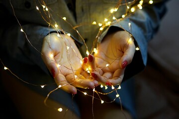 Women's hands and a bright garland with burning lights. The concept of Christmas and New Year holidays.