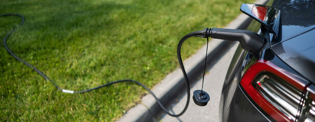 Black electric car charging outdoors in summer.