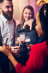 People hands holding flute glasses while pouring champagne