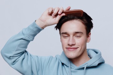 Horizontal portrait photo .a good-looking young man in a light light blue hoodie, combs his head with a comb place in the background to insert an advertising layout