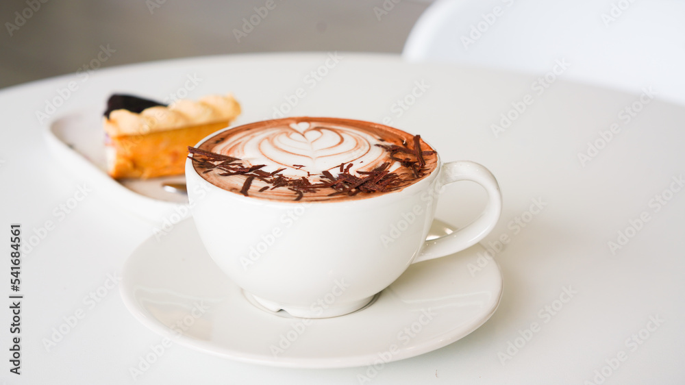 Wall mural Latte art hot coffee with tulip milk latte art on top of white ceramic glass set on table in coffee shop Hot chocolate drink with white foam on top in short cup  on white round table.