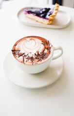 Latte art hot coffee with tulip milk latte art on top of white ceramic glass set on table in coffee shop Hot chocolate drink with white foam on top in short cup  on white round table.