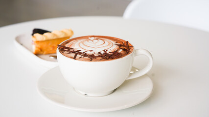 Latte art hot coffee with tulip milk latte art on top of white ceramic glass set on table in coffee shop Hot chocolate drink with white foam on top in short cup  on white round table.
