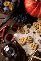 Cookies in the shape of pumpkins and ghosts are in a plate on the table. Next to a teapot and mugs, an autumn still life