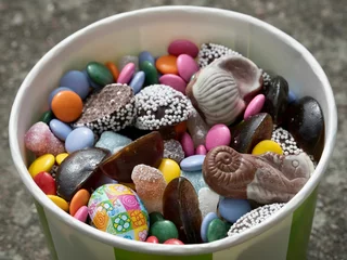 Rolgordijnen Closeup shot of a paper cup filled with chocolates and candies of various forms and colors © Photokrisan/Wirestock Creators