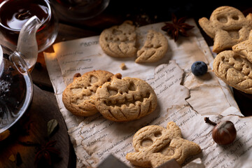 Cookies in the shape of pumpkins and ghosts are in a plate on the table. Next to a teapot and mugs, an autumn still life